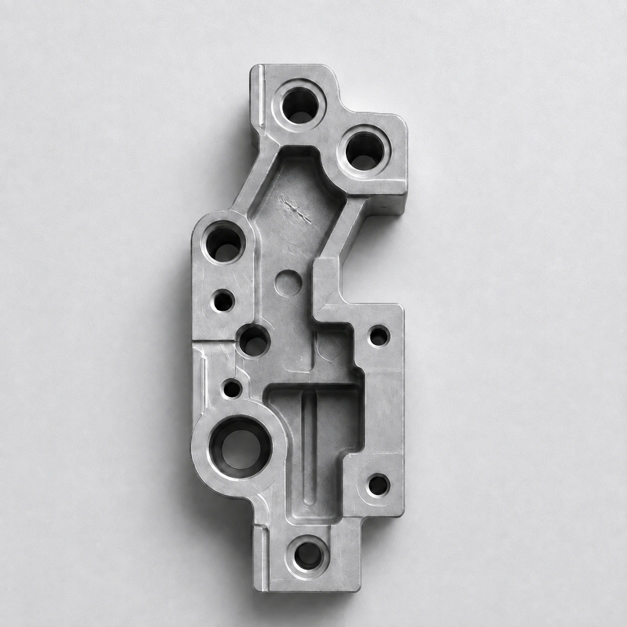 A top-down capture of a machined aluminium bracket with one localized gouge in its upper pocket.